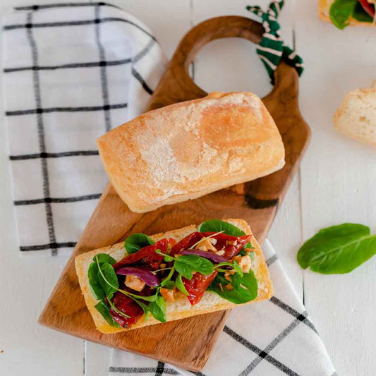 Pao-Ciabatta-inteiro-ao-lado-de-outro-igual-cortado-ao-meio-com-uma-salada-de-folhas-e-tomate-seco-por-cima