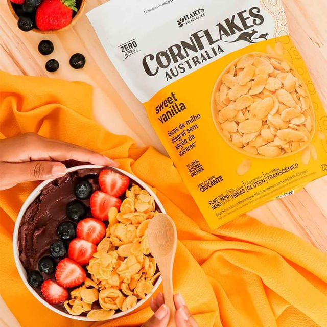 Pacote-de-Cereal-Matinal-Sem-Acucar-ao-lado-de-tigela-com-acai-morangos-mirtilos-e-flocos-crocantes-sobre-pano-amarelo.