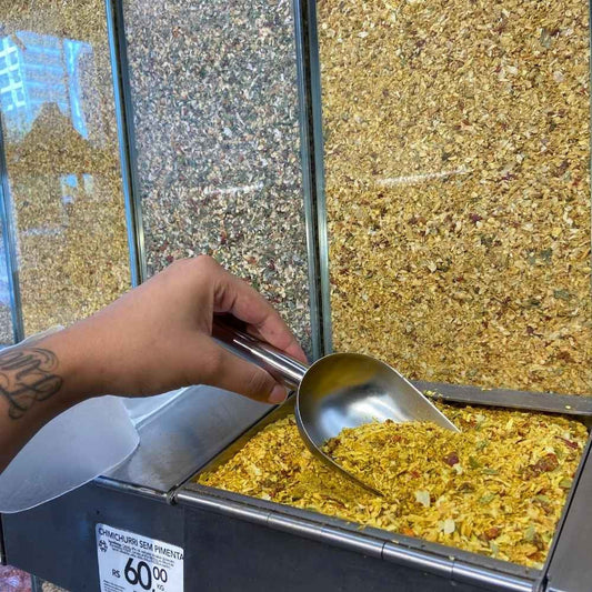 Mao-segurando-uma-colher-de-metal-dentro-de-um-recipiente-com-tempero-pega-marido-a-granel-destacando-sua-coloracao-dourada-e-ingredientes-naturais