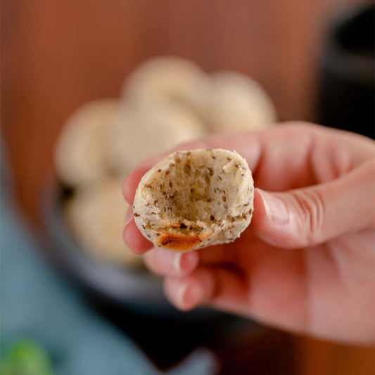 Mao-segurando-um-pao-de-batata-doce-com-chia-com-a-aparencia-proxima-a-de-um-pao-de-queijo-com-uma-mordida